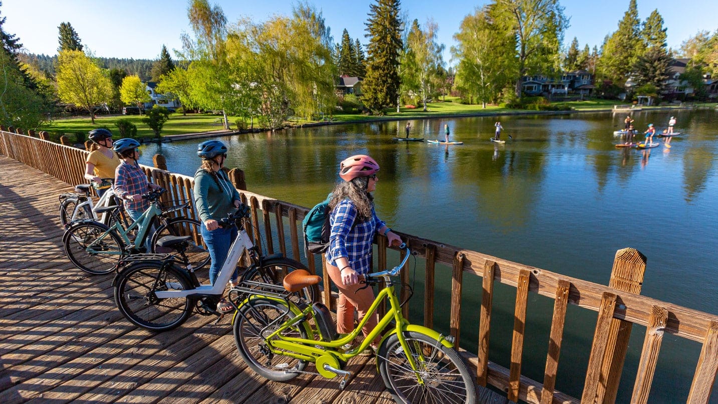 A family of cyclists stand on a bridge looking out at a lake
