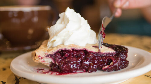 slice of berry pie with fork and whipped cream