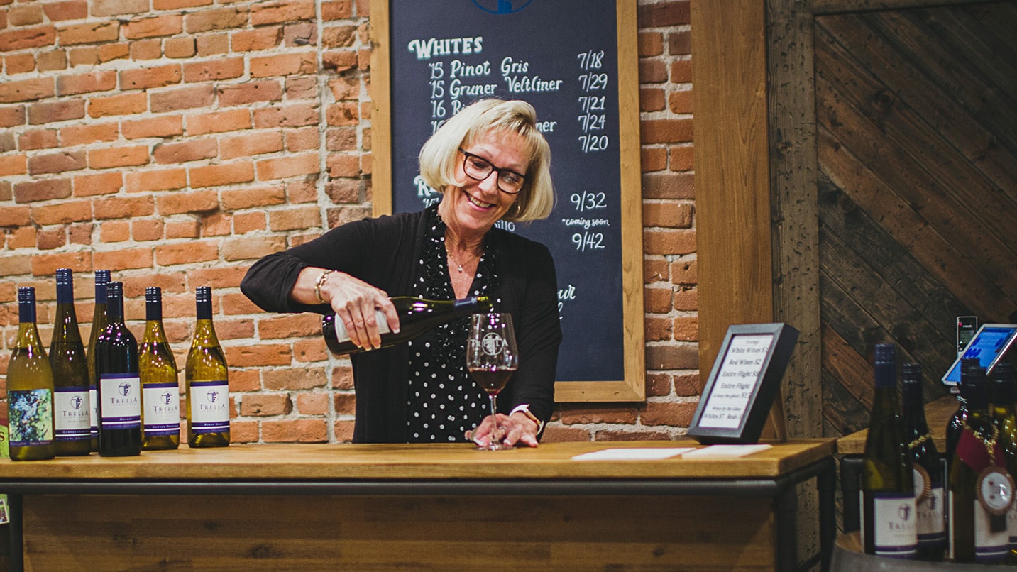 woman pouring wine behind counter