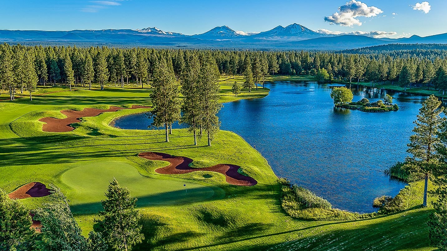 A green golf course with a lake and mountains in the distance
