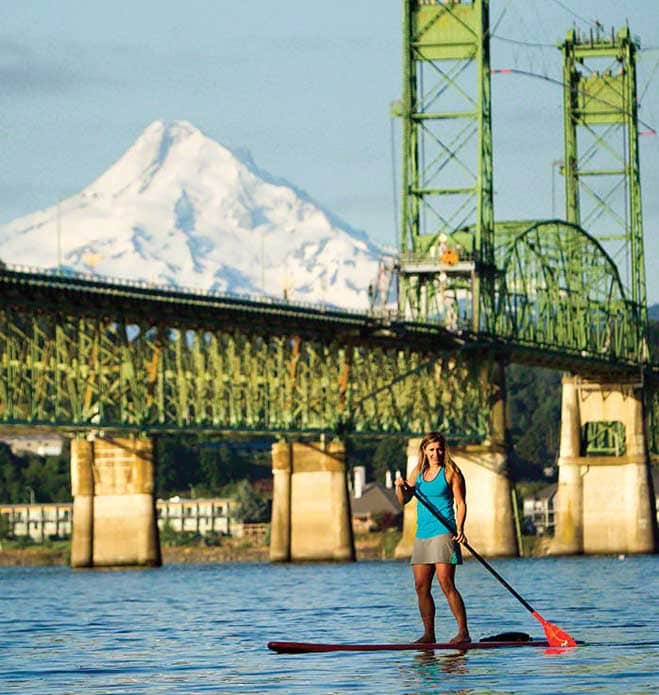 A woman standup paddling boarding on the Columbia River with Mt. Hood in the background. 