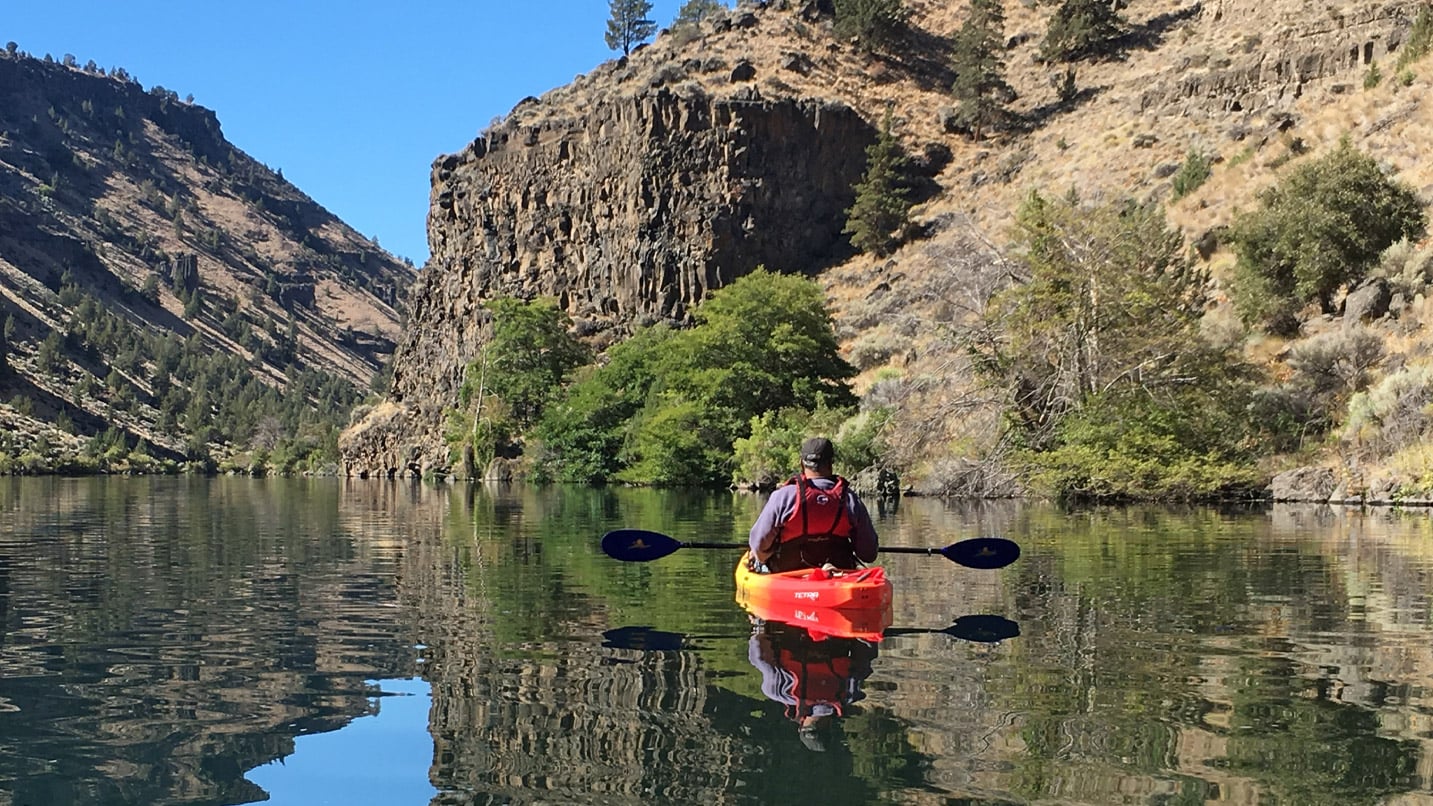 person in kayak on water with mountains reflected in water