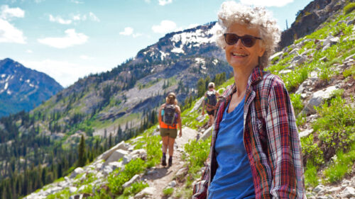 woman smiles at camera with trail and mountains in background