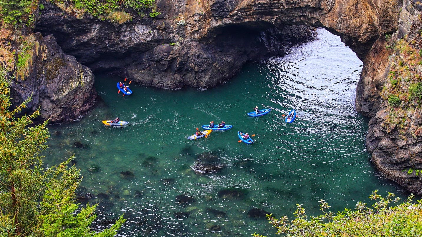 several kayaks in blue water under arch in ocean