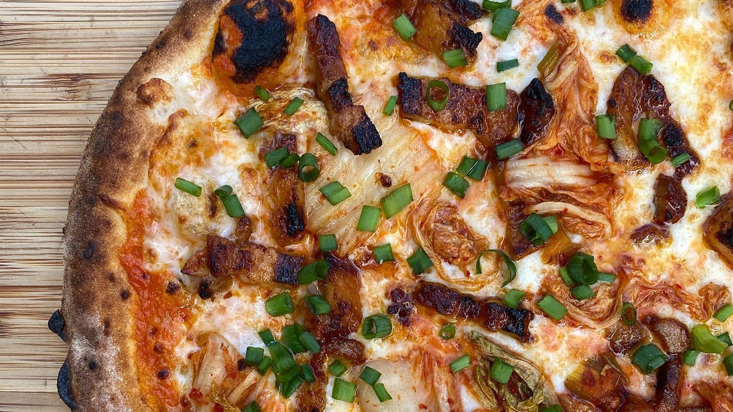 Zoomed in shot of pizza topped with bacon and green onions.