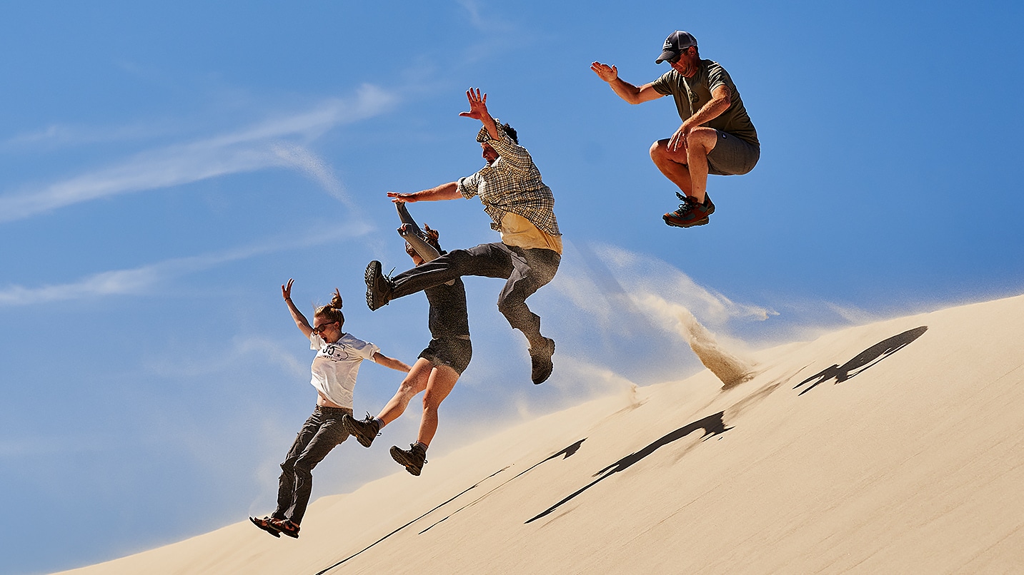 people jump downhill on a sand dune
