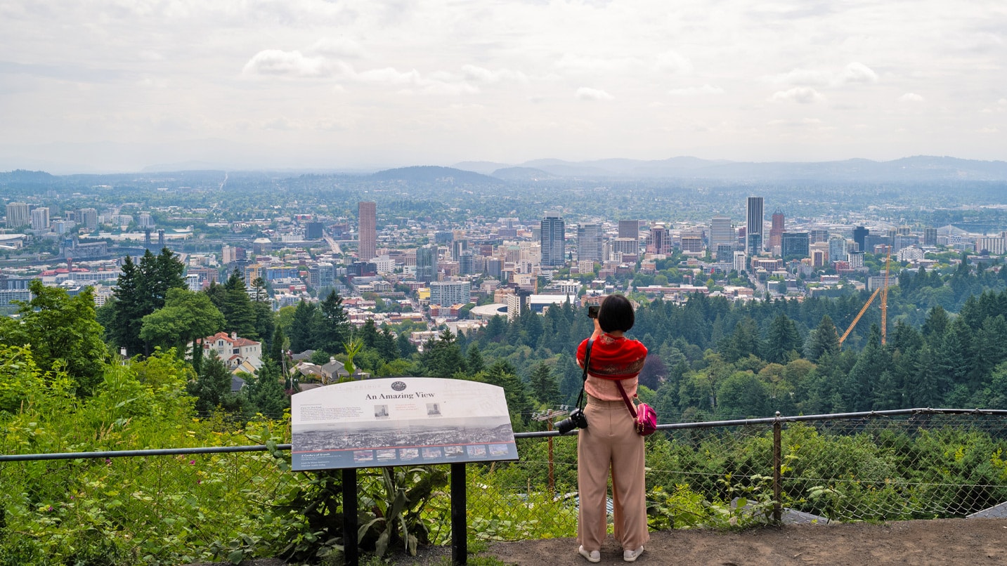 A woman takes a photo of Portland's skyline from a trail stop in Forest Park.