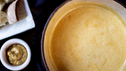 Overhead view of a pot of melted fondue cheese and sides.
