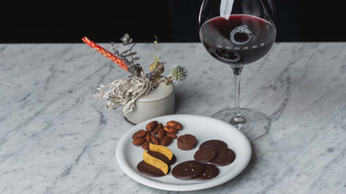 A set up shot of a glass of wine and snack platter of nuts and chocolate.