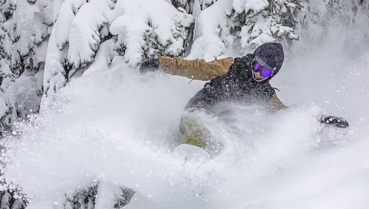 A snowboarder riding through powder. 