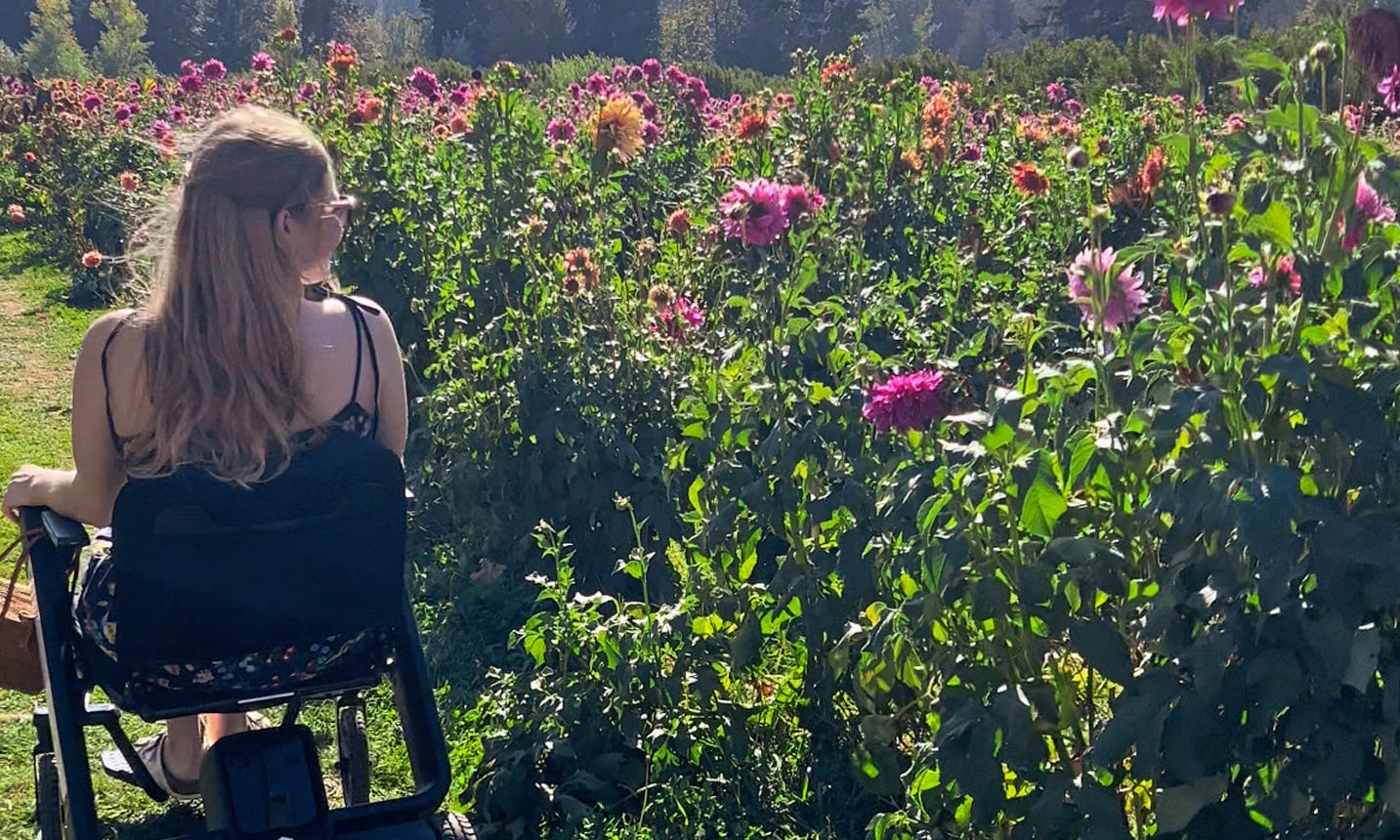 A woman in a wheelchair stops by a field of tall flowers.