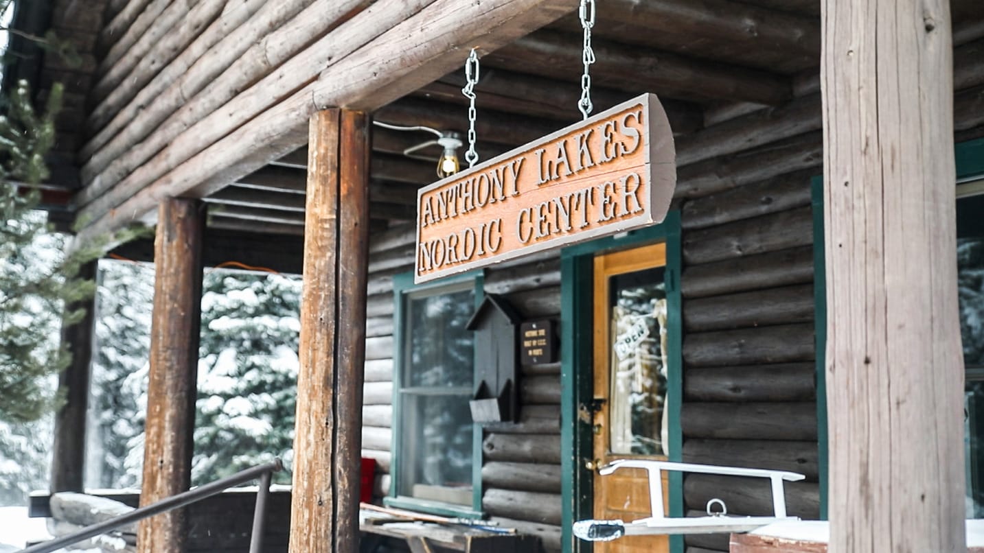 A close up shot of a wooden sign hanging from the entrance of a wooden log cabin.