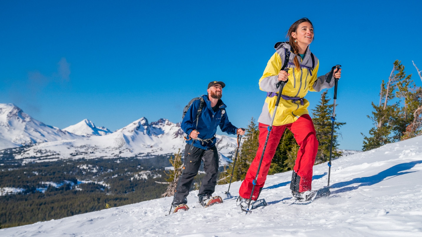 A woman and a man hike on snowshoes with smiles on their faces.