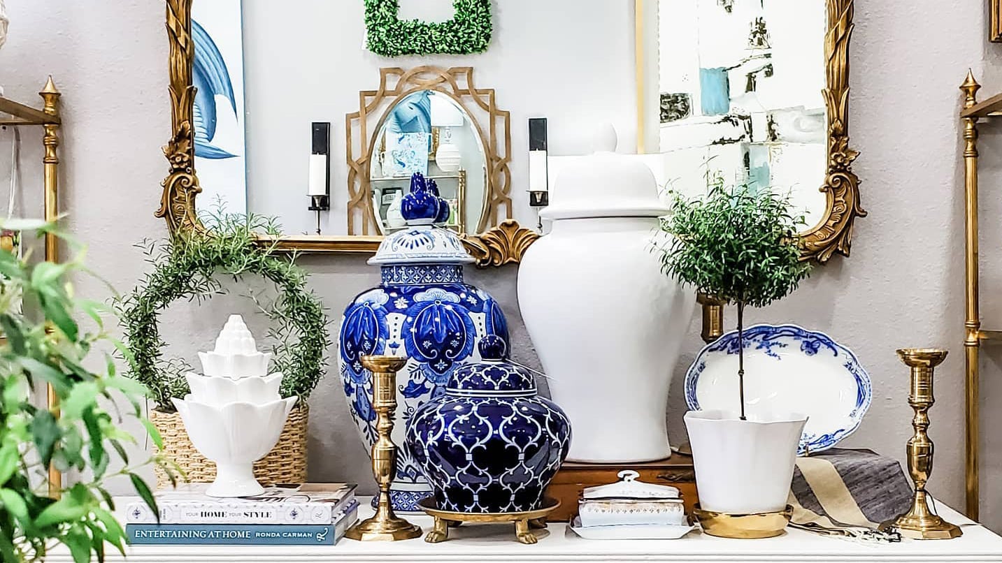 Elaborately painted blue vases, gold candleholders, faux plants and other small knickknacks arranged decoratively on a table top.
