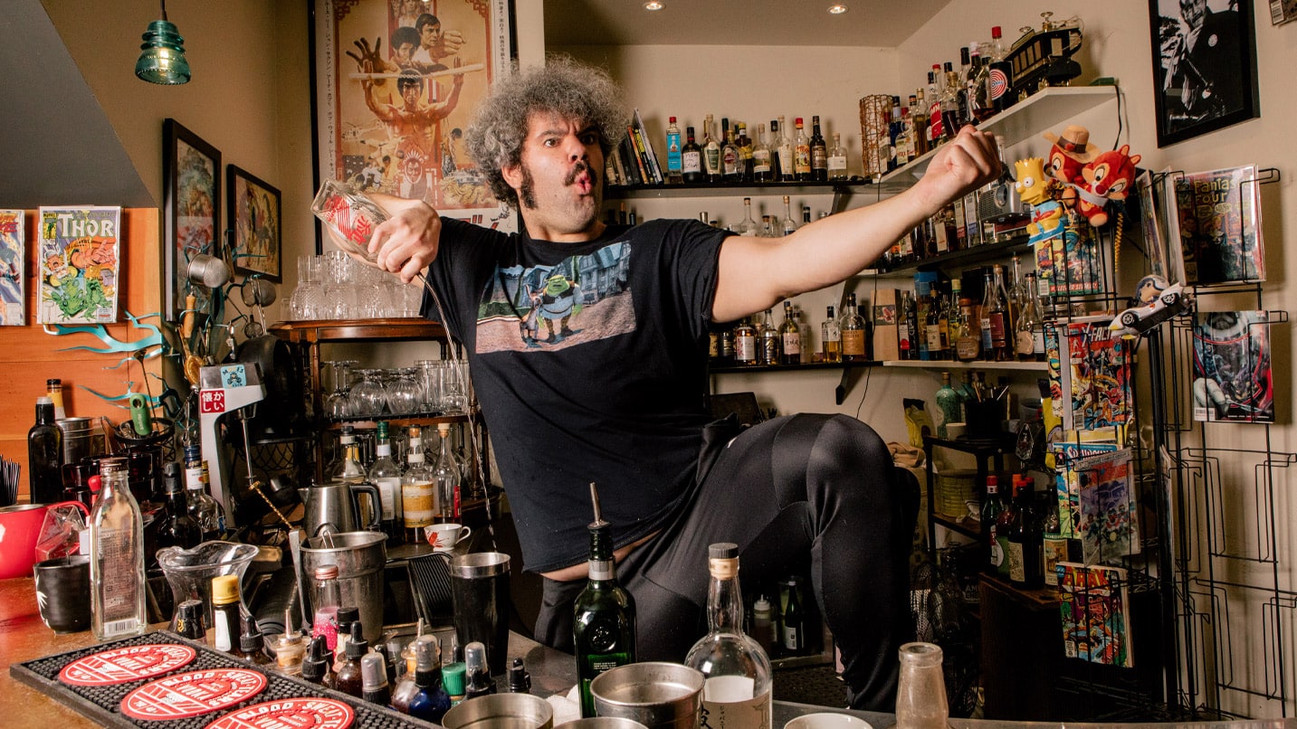 A man poses in a fighting stance as he pour liquor into a tumbler.