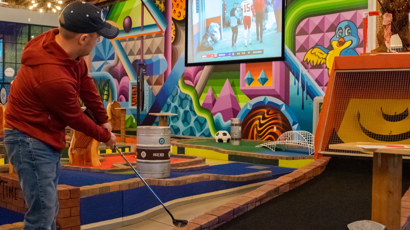 A person plays a hole of mini golf in a colorful setting.