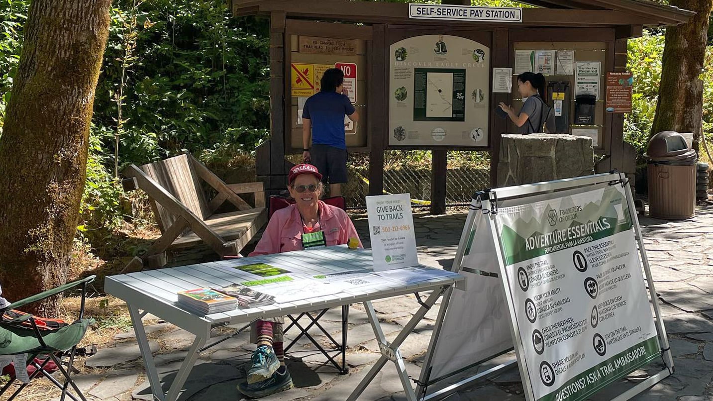 A volunteer smiles from a volunteer information station outdoors.