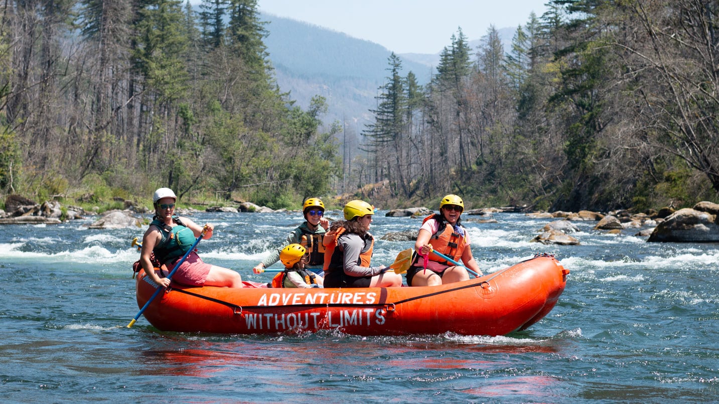 People wear helmets in a bright orange raft on a river.