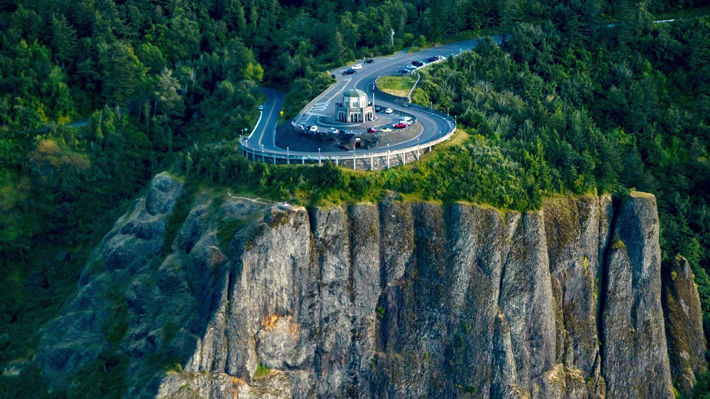 Visitor center with dome atop a tall cliff, with winding road in the background.