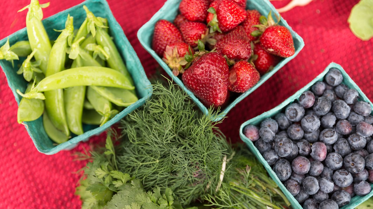 A close up shot of fresh fruits and veggies in containers, including strawberries, blueberries, green beans and dill.