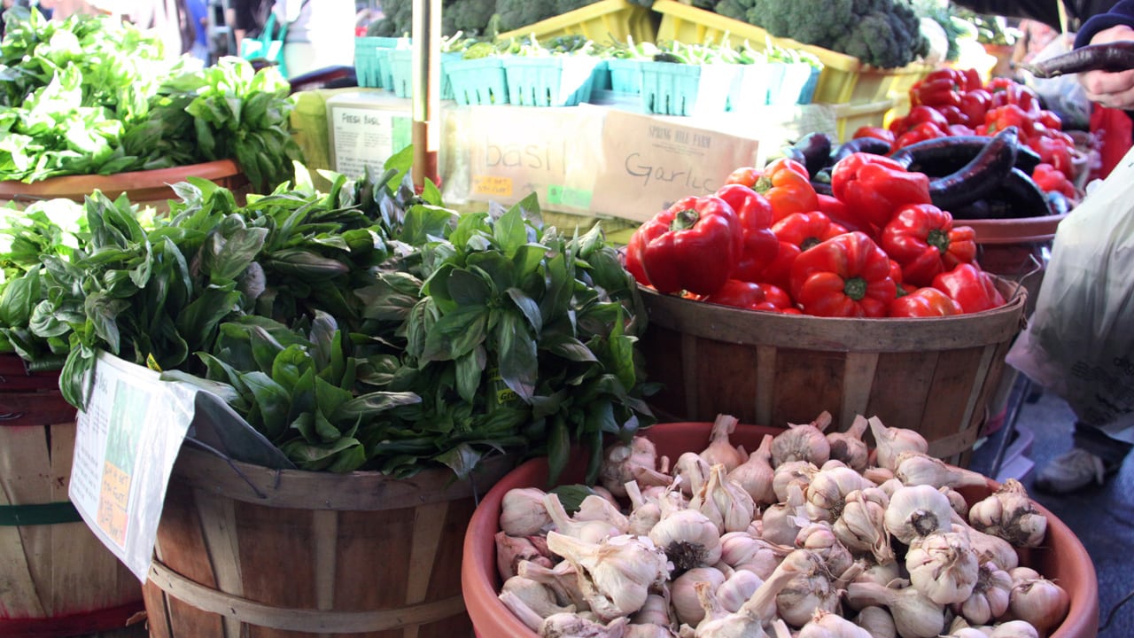 A display at a stand of baskets of basil, red bell peppers and garlic.