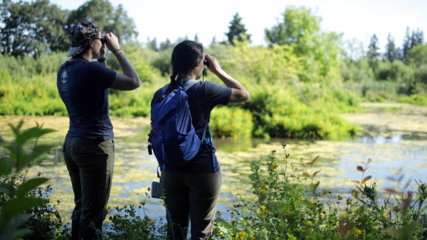 Two women looking out to a pond with binoculars.