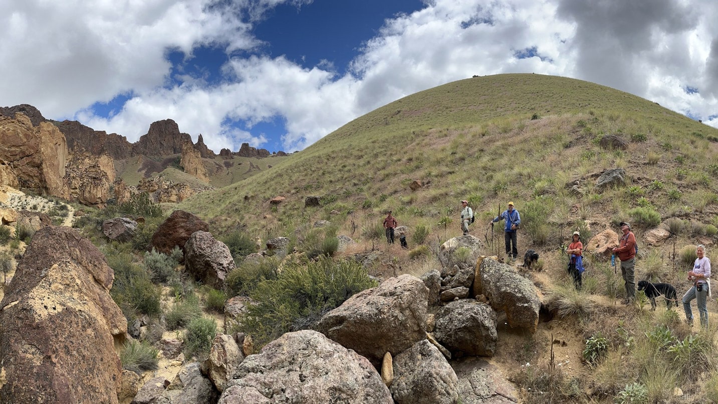 A group of hikers and a dog along a grassy trail of the Owyhee Canyonlands