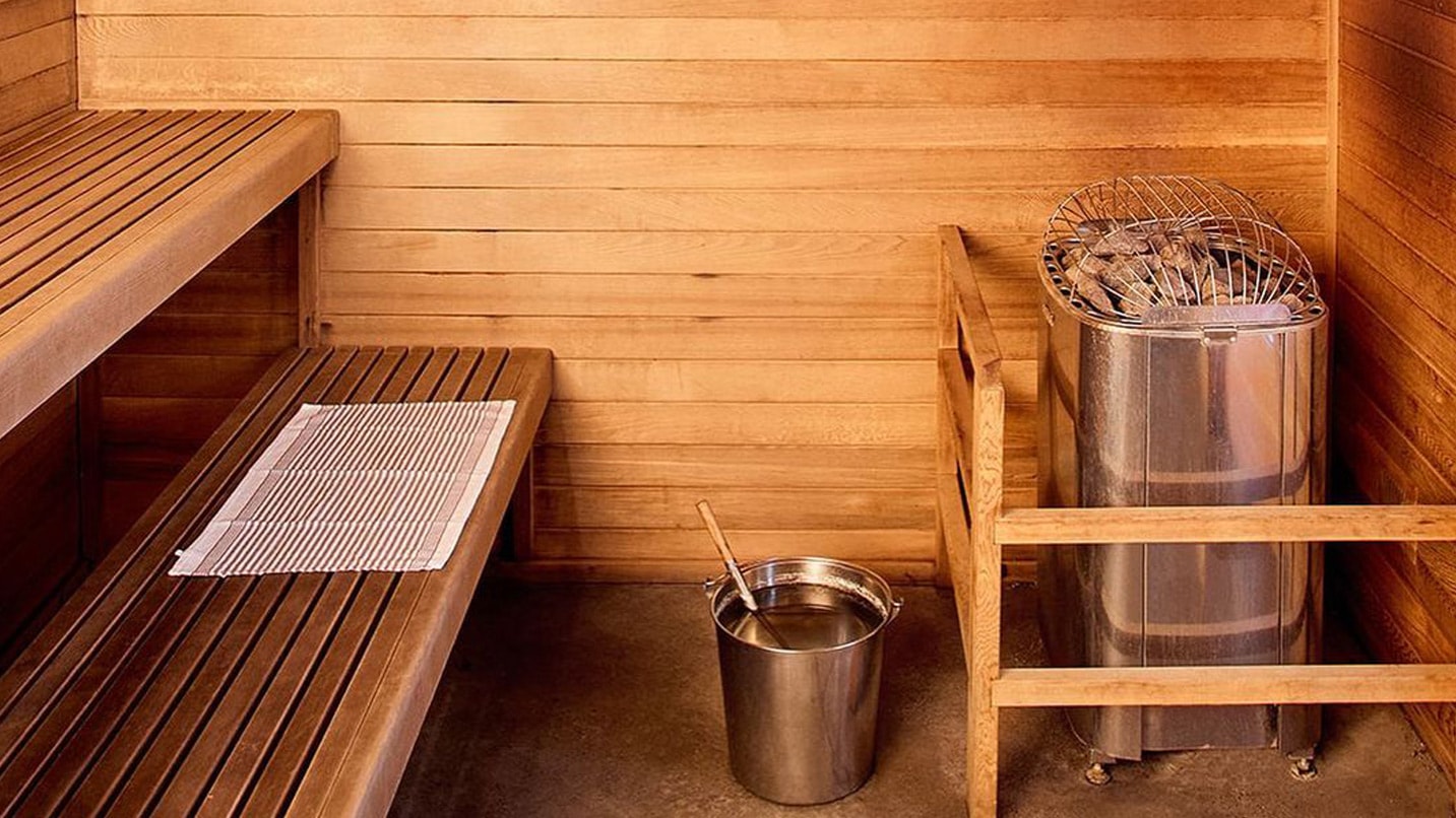 Inside a private sauna, with a wooden bench and wood-fired heater.
