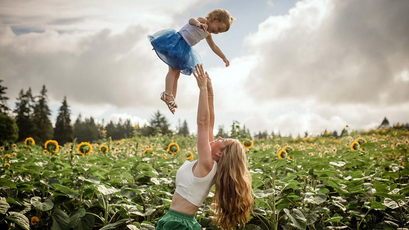 A woman tosses a toddler in the air in a field of sunflowers.