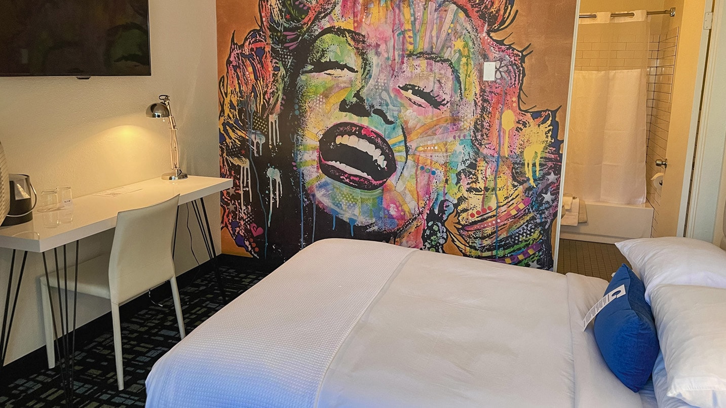 Inside of a hotel room with a giant wall-sized multi-colored mural of Marylin Monroe's face.