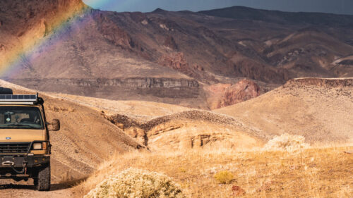 A jeep driving through rugged terrain framed by a rainbow.