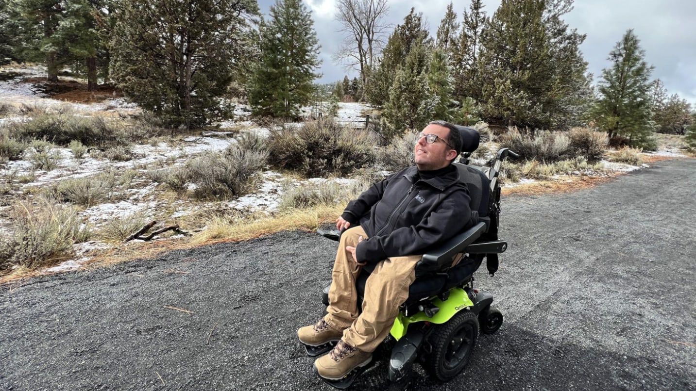 Man in wheelchair on gravel path with trees in background