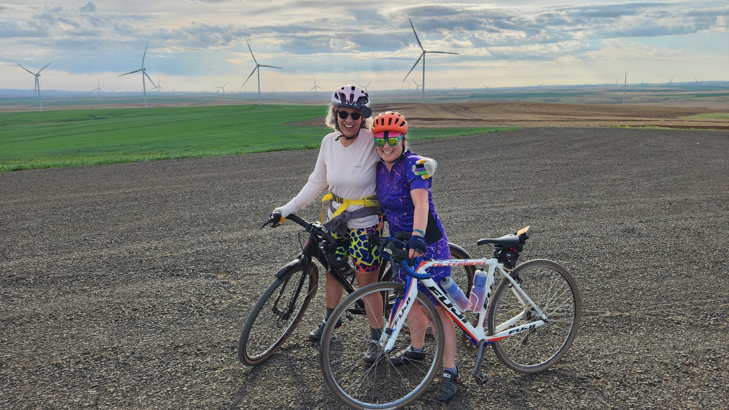 two cyclists standing with bikes with wind turbines in the background