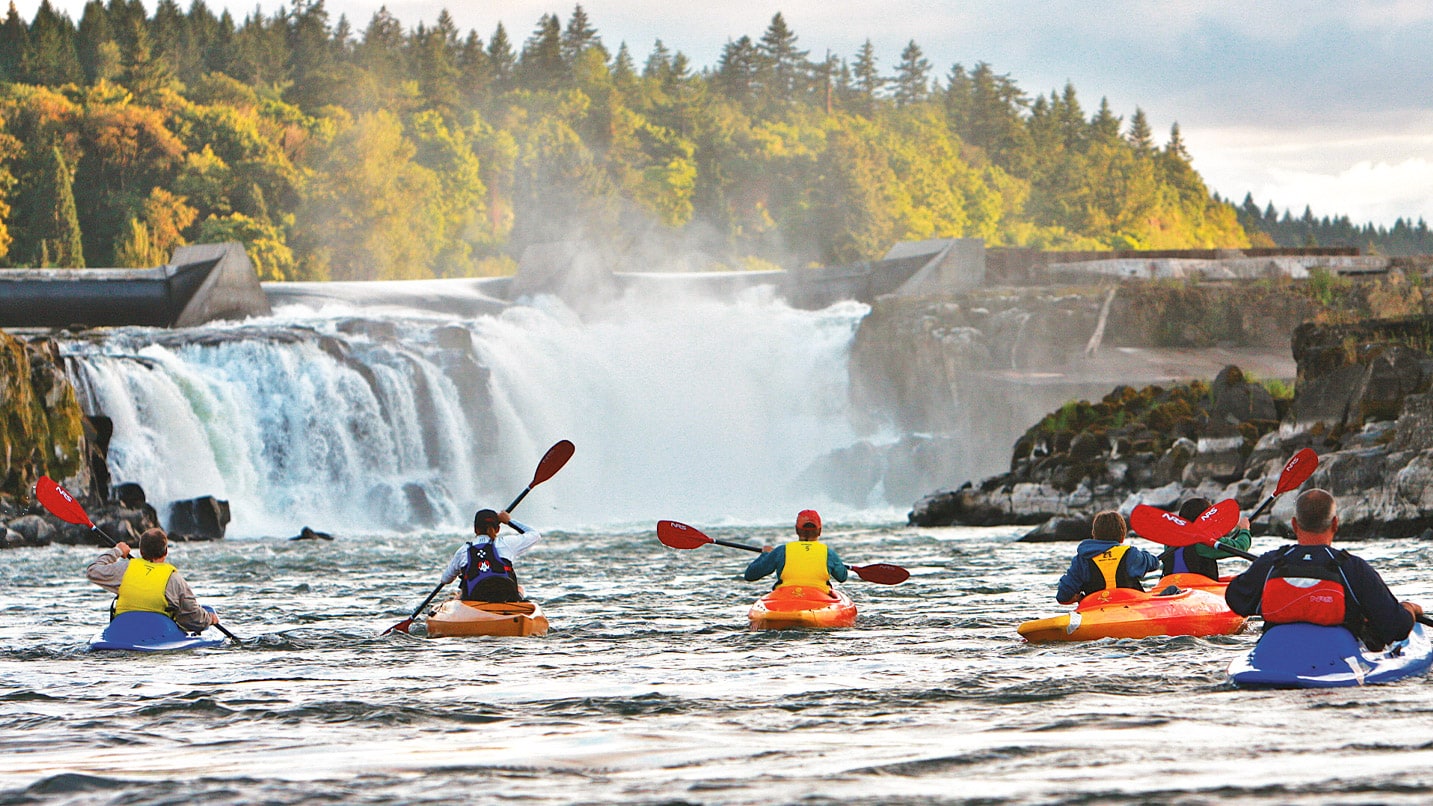 Kayakers on the Willamette River looking towards a waterfall from a dam.