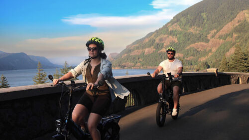 Two cyclists on electric bikes on a paved road along the Columbia River Gorge