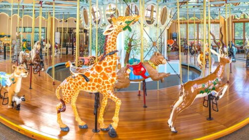 An indoor, brightly painted carousel with exotic animals, including a giraffe, gazelle, panther and bear.