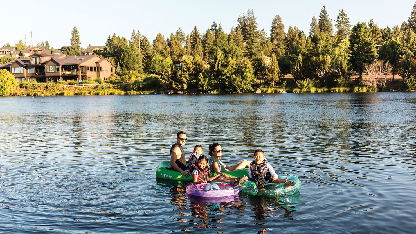 A family of 5 floating on inner tubes on a body of water.