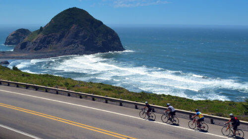 four cyclists on road with ocean and rocky bluff in background