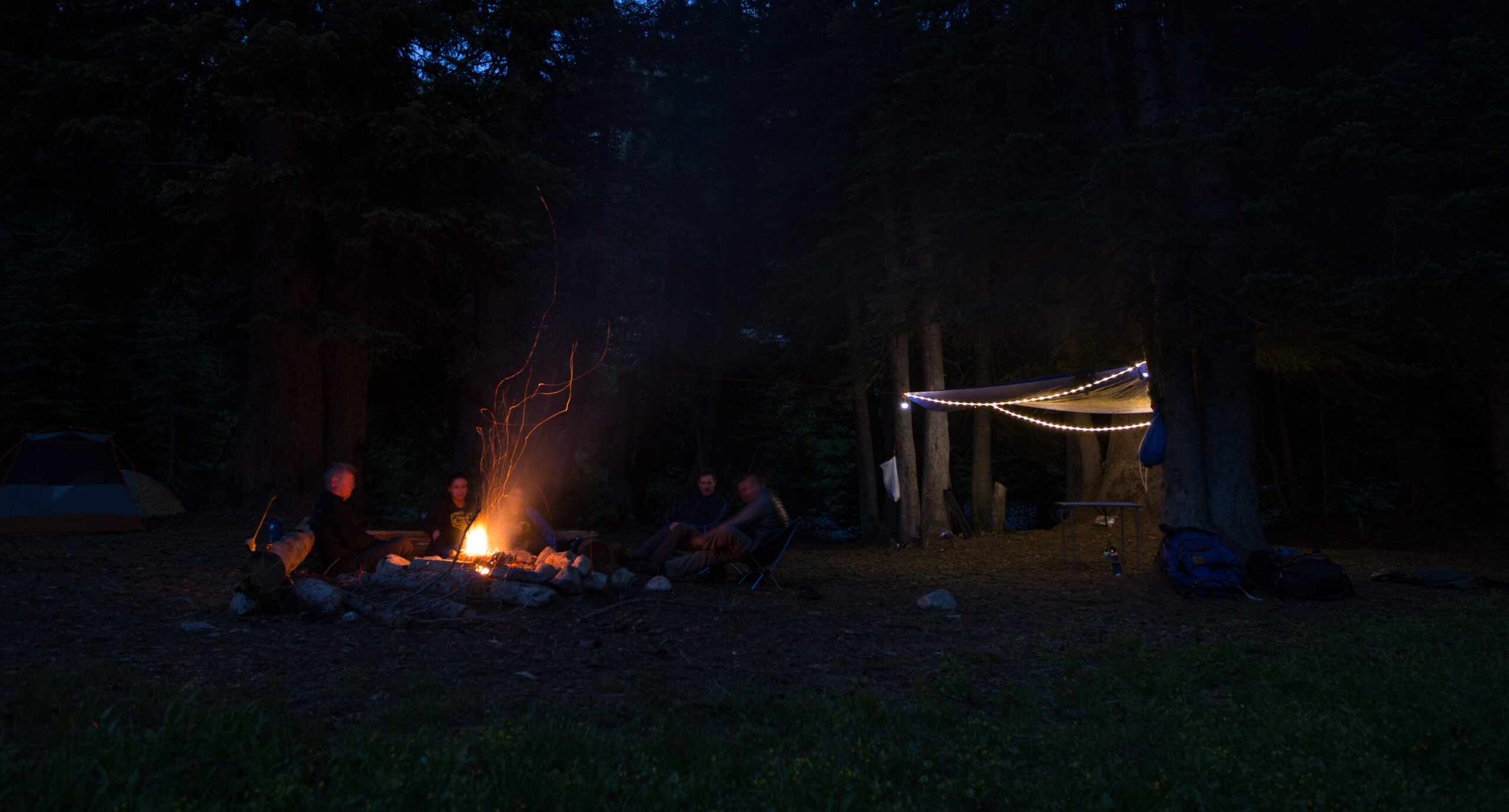 people sit by a campfire next to an illuminated canopy