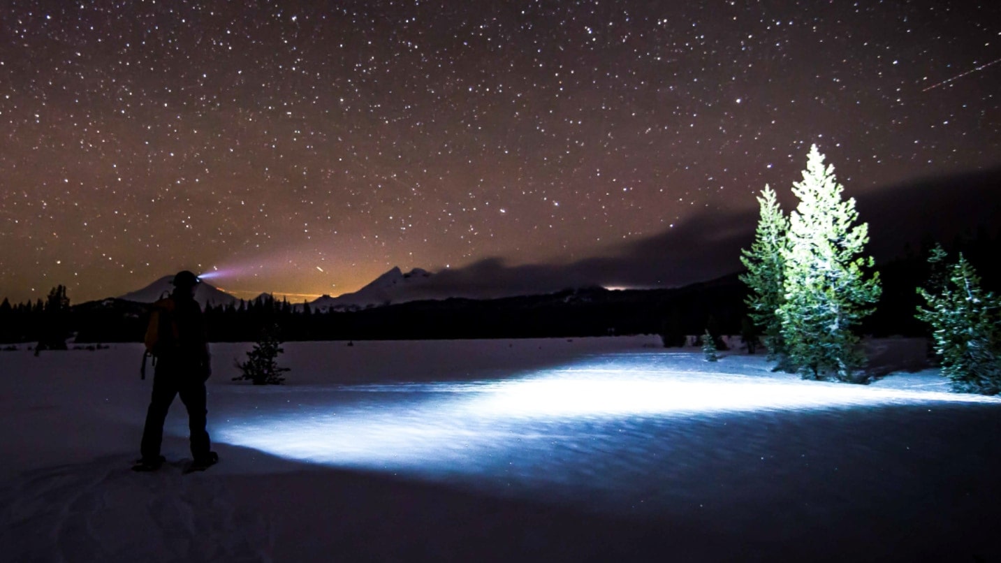 a person with a flashlight on the snow against a starry night sky
