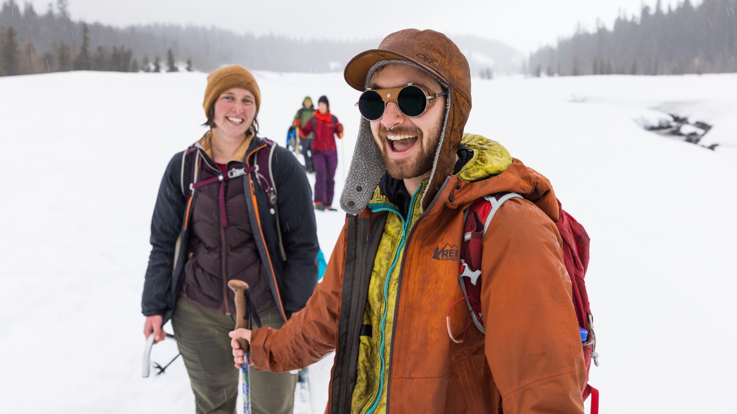 two smiling people wear winter gear in the snow