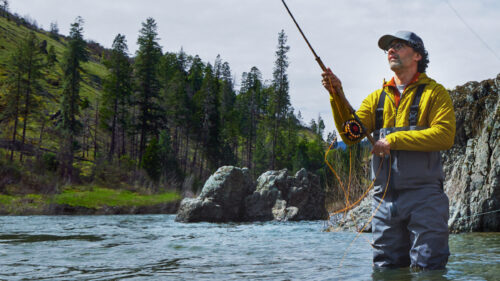 A man fly fishing knee deep in a river.