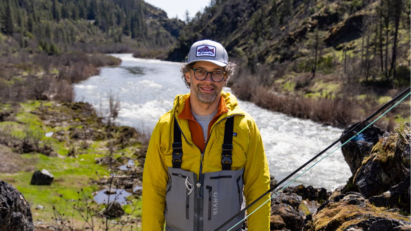 Man in a bright yellow jacket and grey fishing suspenders with the backdrop of the Rogue River.
