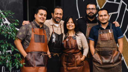 Five people wear leather aprons and smile at the camera