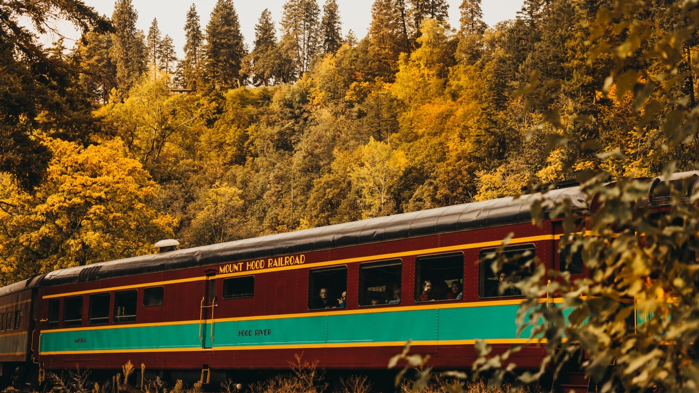 A red train with green stripe against backdrop of yellow-hued trees.
