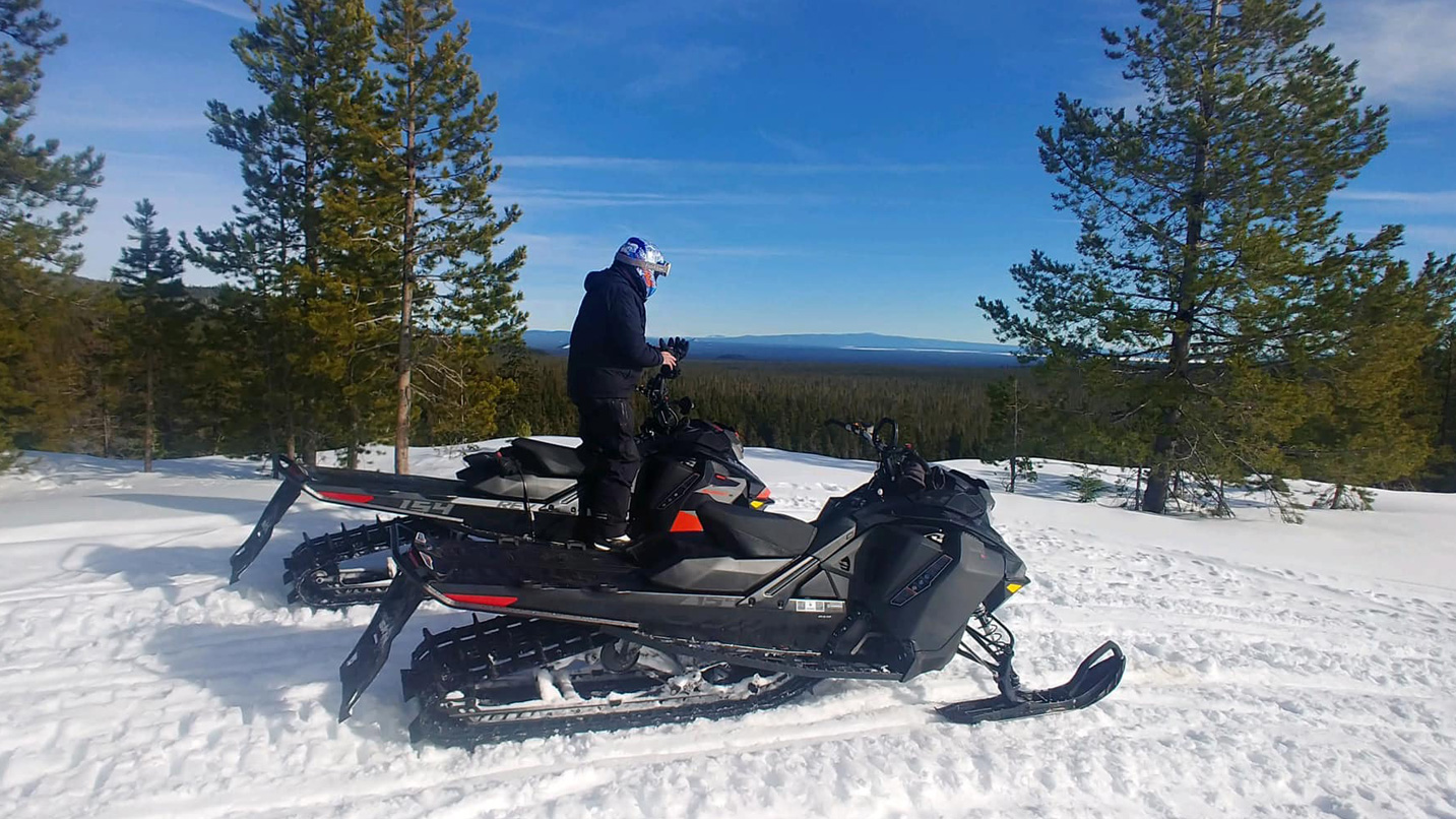 two people on snowmobiles outside on snow.