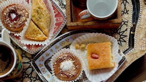 Egyptian pastries, like almond cake and baclava on an adorned plate with coffee.