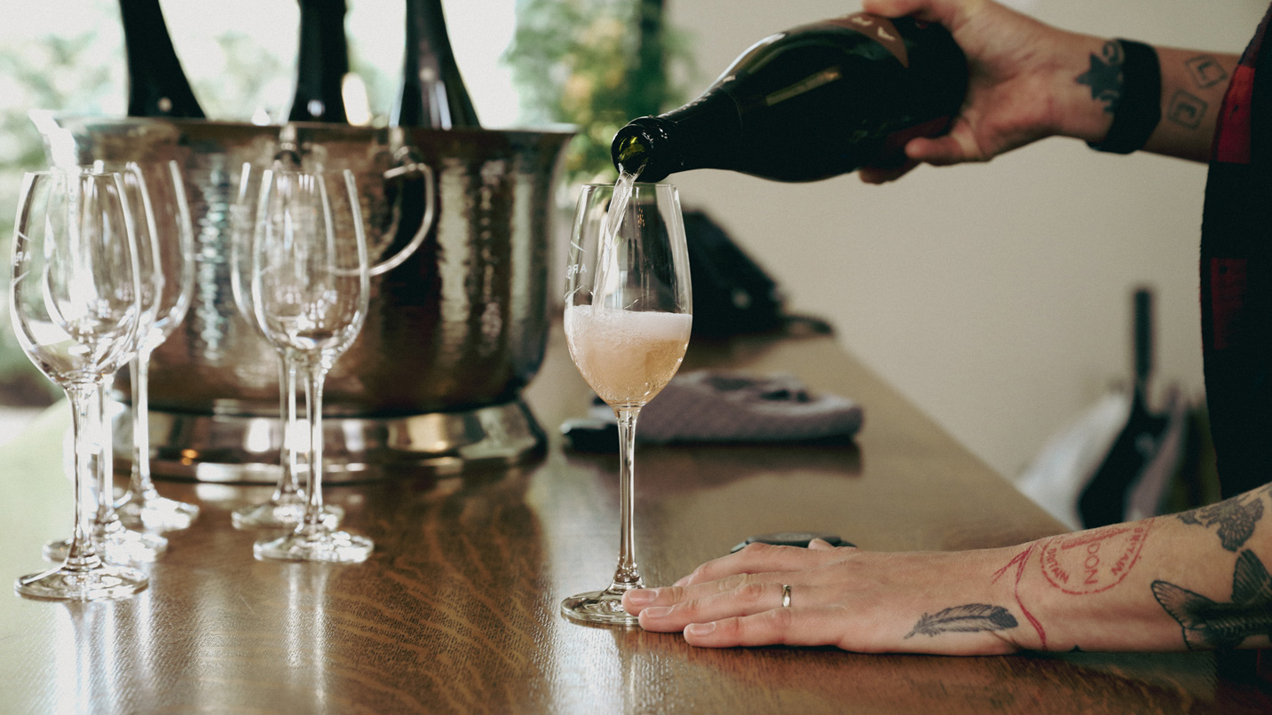 A pair of hands pours a glass of sparkling wine.