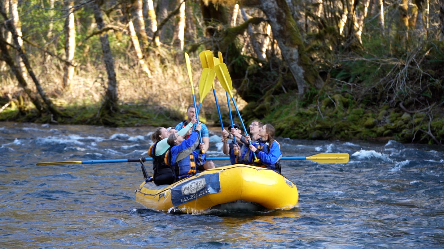 A group of people on a raft on the river high five their paddles together in the air.
