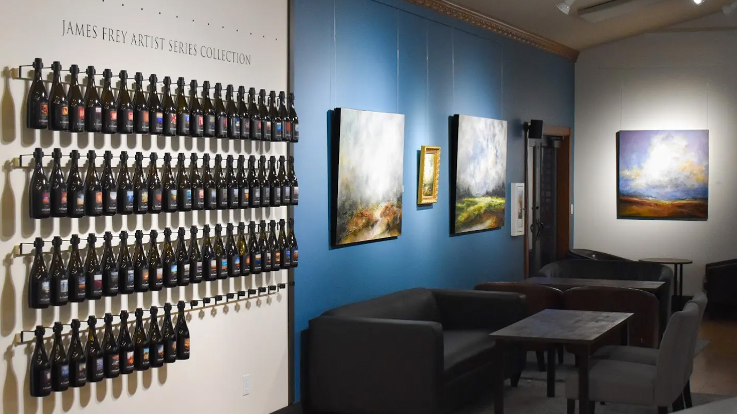 Landscape paintings and a collection of wine bottles on a wall.